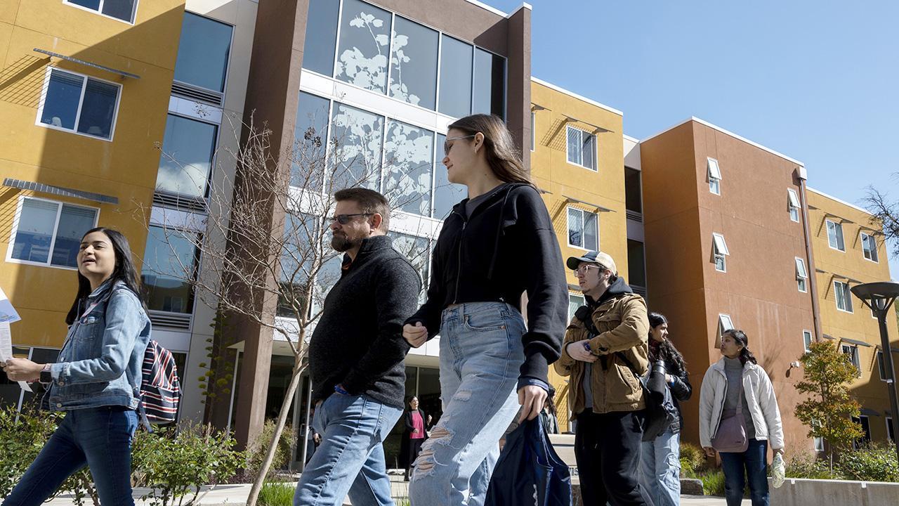 A group of seven students and parents walk in front of residence hall on Aggie Day 2024.